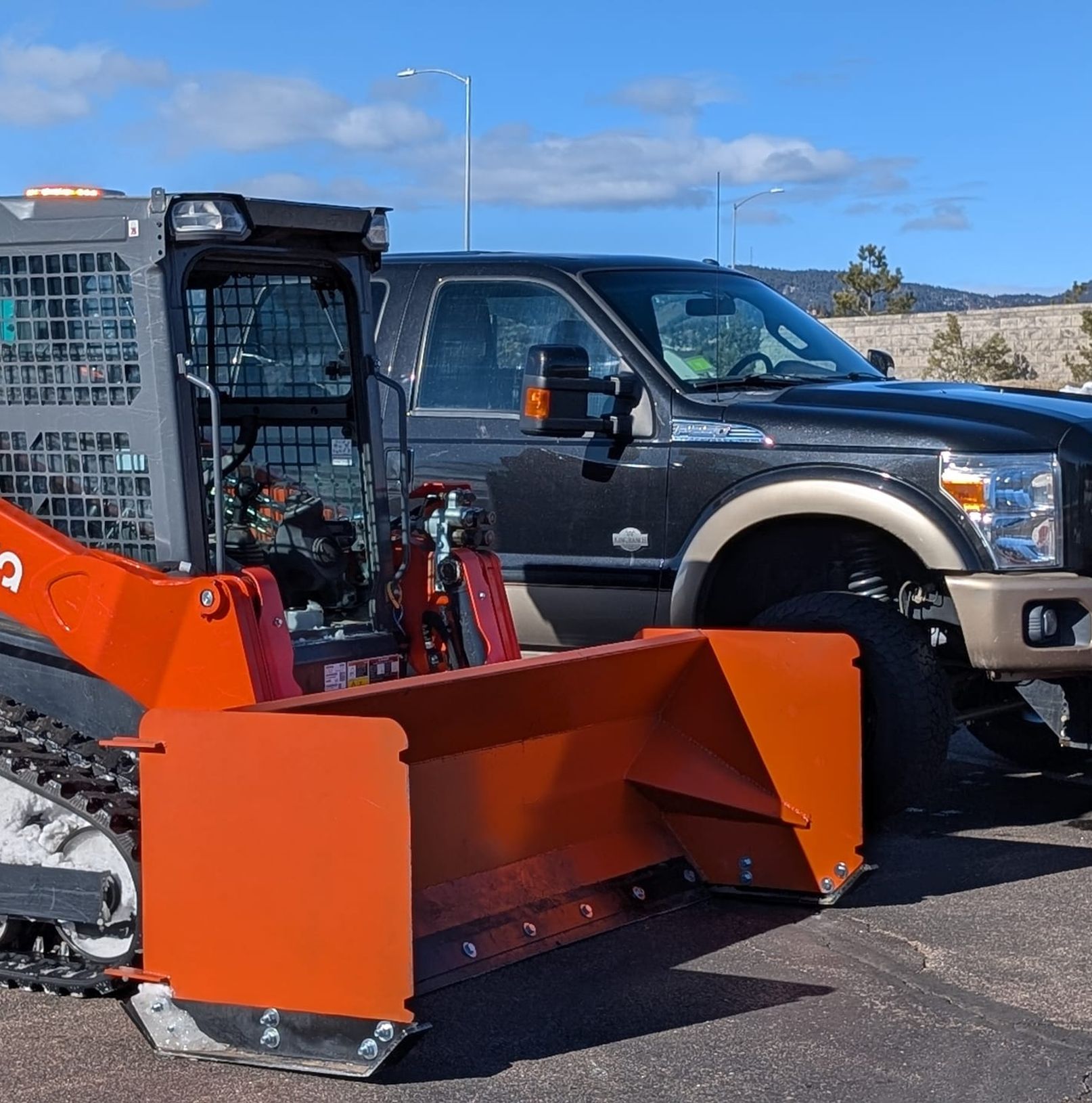 Kubota loader with snow pusher parked beside a plow truck in a cleared lot