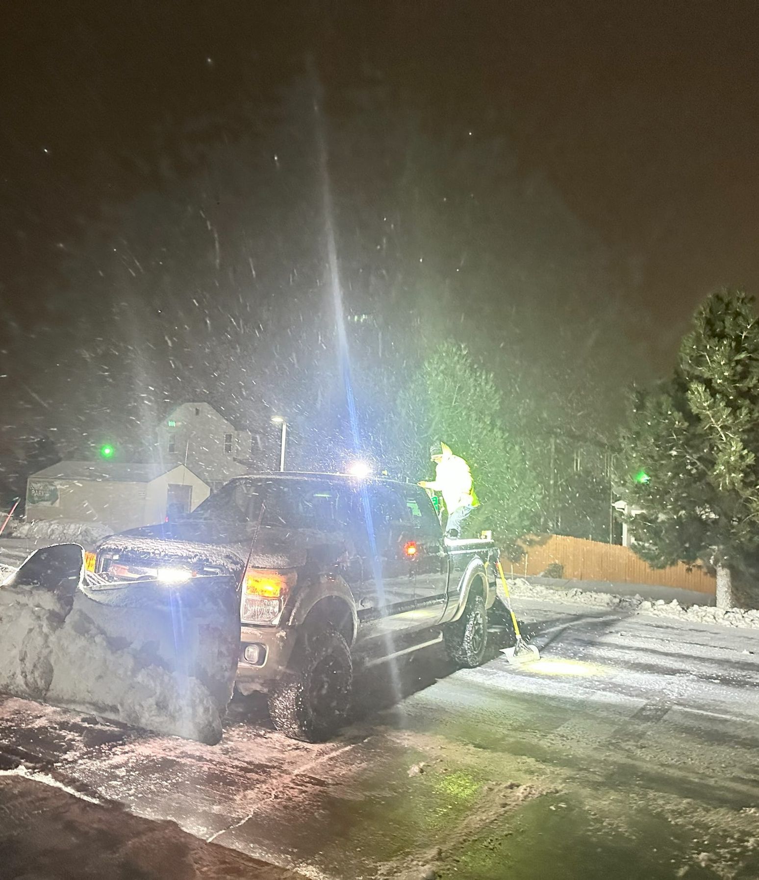 Red Beard's plow truck clearing a commercial lot at night in falling snow